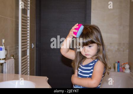 Picture of an adorable little girl combing her hair with a baby brush in the bathroom Stock Photo