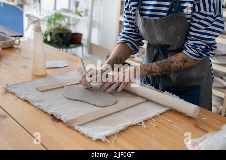 Craft artist making object out of clay in studio, using fettling knife, creating handmade pottery Stock Photo