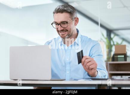 He has some budget available to spend on his business. a mature businessman using a laptop and credit card in an office. Stock Photo