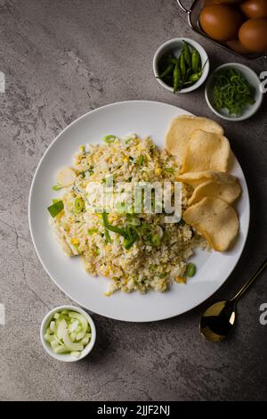 Fried rice or nasi goreng kampung, with scrambled egg, spring onion and cracker on white plate Stock Photo