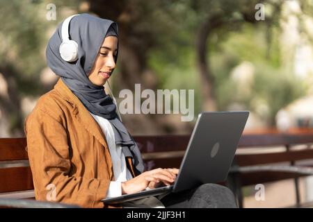 Muslim woman using a laptop while sitting on a park Stock Photo