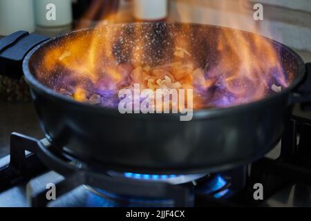 Beef meat fried with onions in frying pan, flambe on gas stove Stock Photo