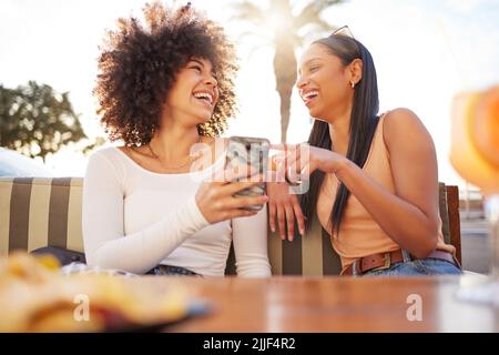 Please send that to me. two friends sharing a funny moment while using a cellphone and having drinks. Stock Photo