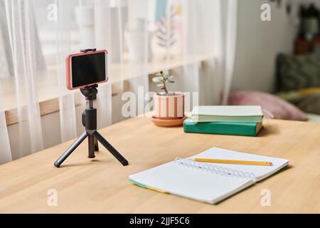 Close-up of mobile phone on tripod for online studying on desk with notebook in teenage room Stock Photo