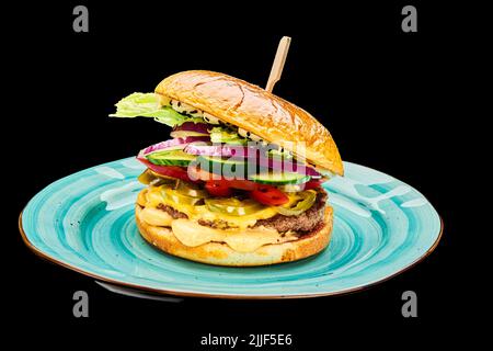 Juicy bbq burger with cheese, tomatoes, red onion, cucumber lies on a blue plate on a black isolated background Stock Photo