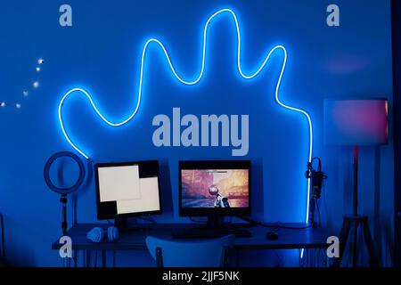 Horizontal image of dark room decorated with neon light and computer monitors on table for video game Stock Photo
