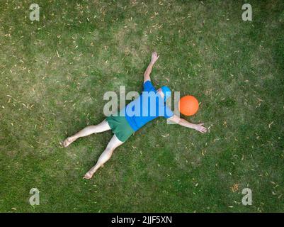 exhausted senior man lying down on a grass and resting after heavy slam ball workout, view from above Stock Photo