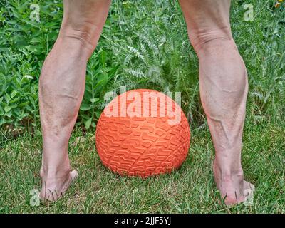 senior man legs and heavy rubber slam ball filled with sand in a backyard, exercise and functional fitness concept Stock Photo