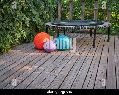 three heavy slam balls filled with sand and mini trampoline on a backyard deck with morning light, exercise, rebounding  and functional fitness concep Stock Photo