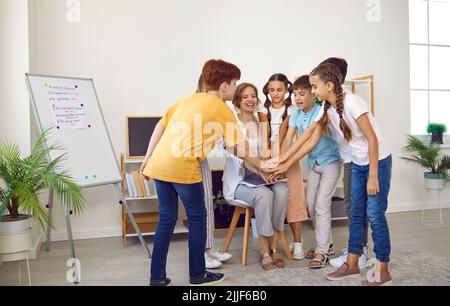Funny elementary school students together with their female teacher are making stack of hands. Stock Photo