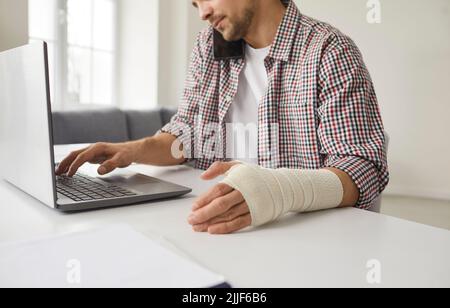 Young man with elastic bandage wrapped around his hand working on laptop computer Stock Photo