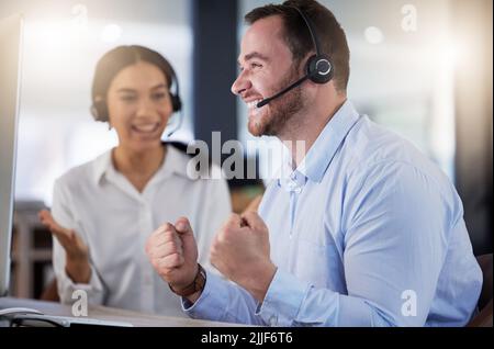 Another target exceeded with ease. a young call centre agent cheering while working on a computer in an office at night. Stock Photo
