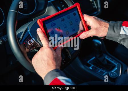 Ato mechanic with mobile tablet for inspecting the electronic systems of cars at the service. Car repair shop Stock Photo