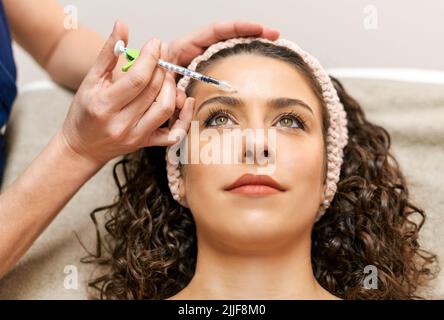 Crop anonymous beautician injecting charming female client with anti age filler during skin care procedure in modern light beauty salon Stock Photo