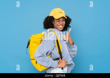 Black woman with backpack winking and pointing finger at camera isolated over blue background Stock Photo