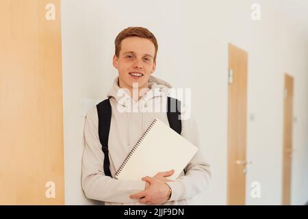 Smiling teenager leaning a wall in high school looking at camera Stock Photo