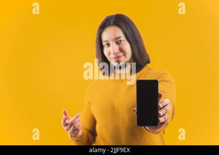 A young bearded hispanic person advertising a phone displayed on a yellow studio background. High quality photo Stock Photo