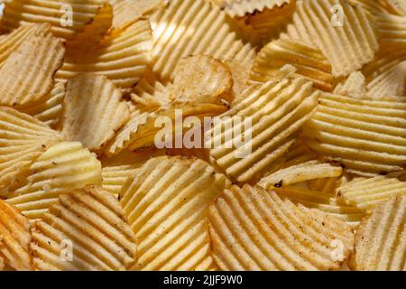 background corrugated golden chips with texture. corrugated chips with salt, spices, with fried barrels, selective focus. daylight, side view, close-u Stock Photo
