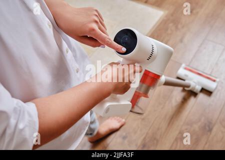Women hands and display control wireless portable vacuum cleaner in the kitchen. A woman cleans the floor in an apartment with a vacuum cleaner with a Stock Photo