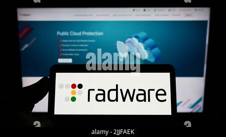 Person holding smartphone with logo of US cybersecurity company Radware Ltd. on screen in front of website. Focus on phone display. Stock Photo