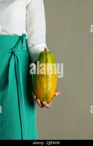 Close-up of a woman holding a papaya against plain background - stock photo Stock Photo