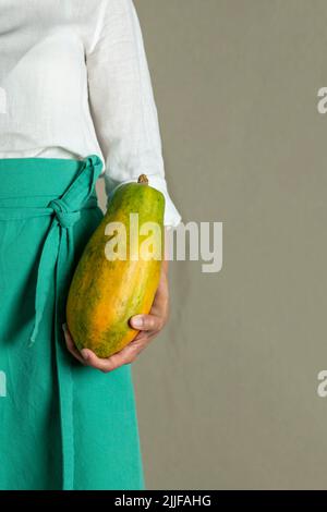 Close-up of a woman holding a papaya against plain background - stock photo Stock Photo