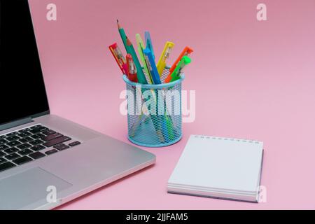 Laptop pens and colored pencils in blue stand and white stickers on pink background, back to school and business education concept Stock Photo