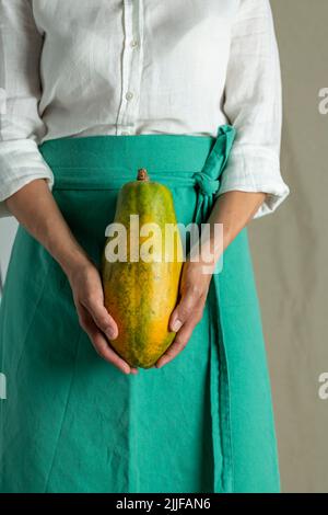 Close-up of a woman holding a papaya against plain background - stock photo Stock Photo