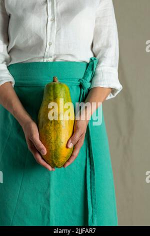 Close-up of a woman holding a papaya against plain background - stock photo Stock Photo