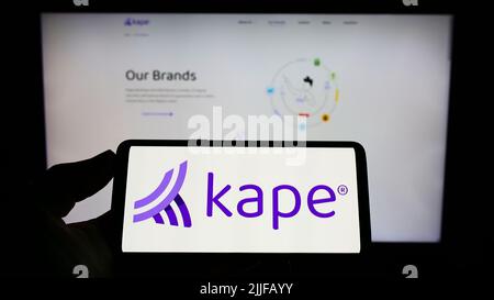 Person holding smartphone with logo of cybersecurity company Kape Technologies plc on screen in front of website. Focus on phone display. Stock Photo