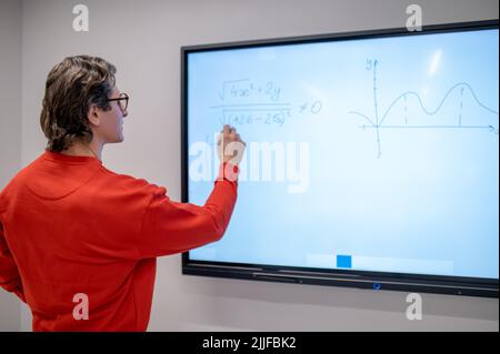 A teacher in red shirt writing on the board at the lesson Stock Photo