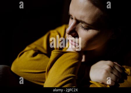 Woman suffering from depression and lying on floor with her hands covering head on black background. Stock Photo