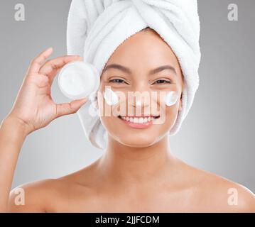 Skin care must be good enough to eat. an attractive young woman applying moisturiser to her face against a studio background. Stock Photo