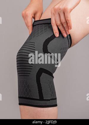 Woman putting on knee brace to support painful leg or heal from injury. Tool used by athlete after trauma for doing sport. Health problems, medical conditions concept. High quality photo Stock Photo