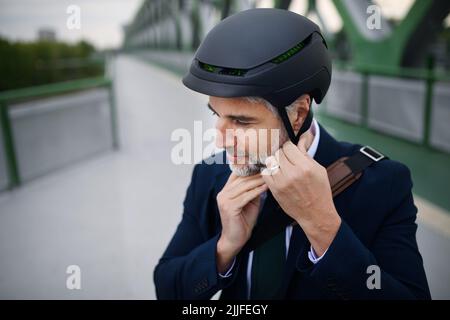 Portrait of businessman commuter on the way to work putting on cycling helmet, sustainable lifestyle concept. Stock Photo