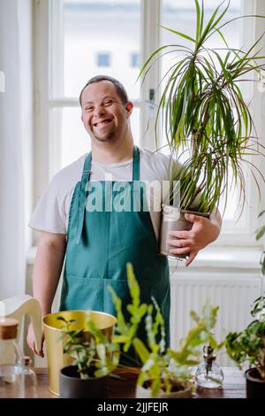 Young man with Down syndrome taking care of plants at home, smiling and looking at camera. Stock Photo