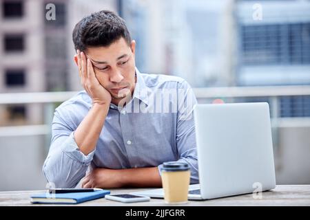 The emails just keep coming. a young businessman looking bored while using a laptop at work. Stock Photo