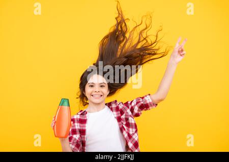 Child teen girl with shampoos conditioners and shower gel. Long hair care of teenager. Presenting cosmetic product, shampoo bottle. Amazed teenager Stock Photo
