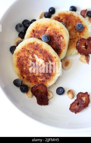 Homemade Breakfast. Traditional Syrniki with Sour Cream, Blueberries, Nuts and Dates Served on White Plate. Stock Photo