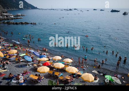 Camogli, Liguria, Italy - June, 2022: People lying on sun loungers under beach umbrellas, sunbathe and swim in Mediterranean sea on coast of Riviere Stock Photo