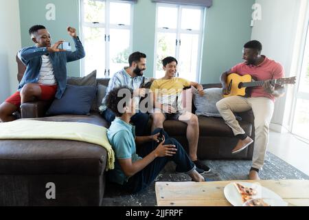 Multiracial friends enjoying beer and using smartphone while looking at young man playing guitar Stock Photo