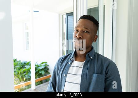 Portrait of confident african american young man wearing jacket standing by window at home Stock Photo