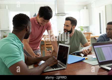 Smiling multiracial male entrepreneur talking with colleagues working at desk in office Stock Photo