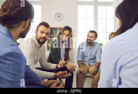 Different men and women at support group meeting listen to young man talking about himself. Stock Photo