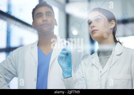 Making sense of it all. two scientists solving equations on a glass screen in a laboratory. Stock Photo