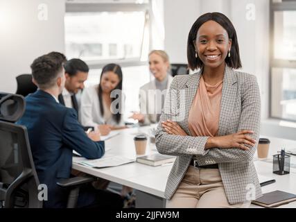 Every new day presents a new opportunity of becoming successful. a young businesswoman standing with her arms crossed in the boardroom with her Stock Photo