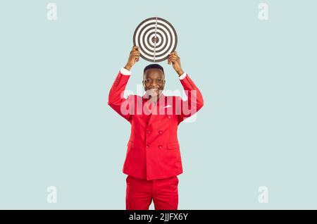 Smiling African American man in stylish red suit who is holding target over his head. Stock Photo
