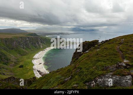 Måtind lookout at a rocky seascape bellow it. View from a mountain top next to the Norway sea with steep cliffs, white sandy beach and a greenery. Stock Photo