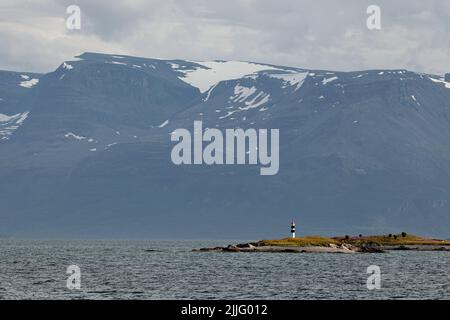 Lighthouse on a small island in Norway with a huge snow covered mountain behind it. Stock Photo