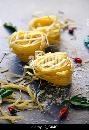 Italian raw fettuccine on a opaque surface with red hot peppers and basil Stock Photo